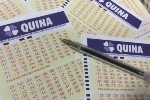 Cartelas de aposta de loteria Quina com números marcados, um bolígrafo posicionado sobre os bilhetes, indicativo de jogo ou aposta na loteria brasileira.