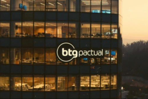 Imagem do prédio da BTG Pactual durante o pôr do sol, com destaque para o logo iluminado de BTG Pactual no edifício moderno de vidro.