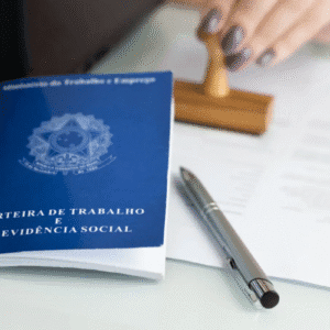 Imagem de uma carteira de trabalho e previdência social sobre uma mesa, com uma caneta e uma mão usando um carimbo ao fundo, representando documentos trabalhistas e previdenciários.