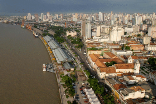 Vista aérea de um rio urbano com edifícios modernos e históricos, mostrando a cidade de alta densidade populacional com uma paisagem urbana vibrante em dia nublado.