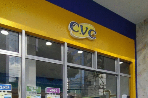 Fachada de uma loja CVC com logo amarelo e azul, destaque para a entrada de vidro e cartazes informativos na frente, localizada no Brasil.
