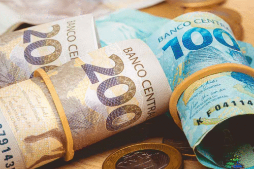 Imagem de várias cédulas de dinheiro brasileiro, incluindo real de 20 e 100, e moedas, simbolizando riqueza e economia no Brasil.