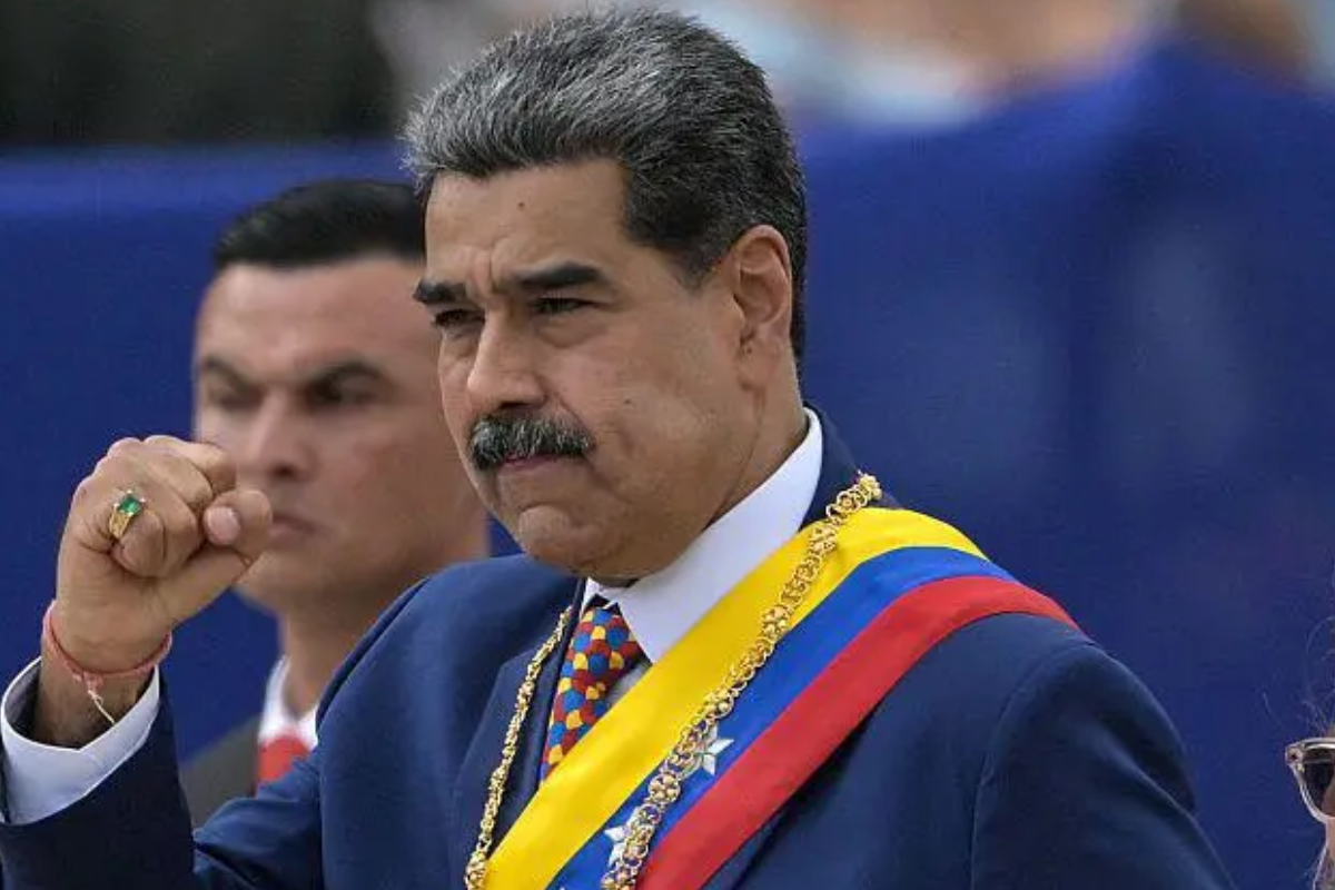 Imagem de Nicolás Maduro, presidente da Venezuela, durante uma cerimônia oficial, usando terno azul e uma faixa presidencial nas cores da bandeira venezuelana.