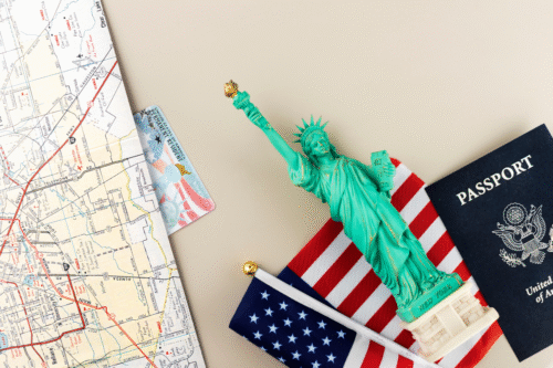 Imagem com itens de viagem incluindo mapa de transporte público, mini Estátua da Liberdade, bandeiras dos EUA e passaporte, representando preparação para viagem aos Estados Unidos.