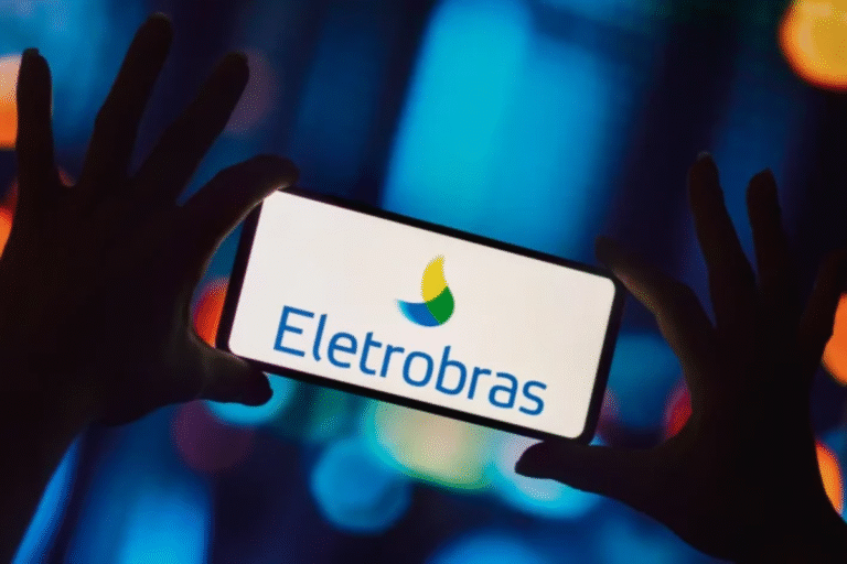 Pessoa segurando um celular exibindo o logotipo da Eletrobras, empresa de energia elétrica no Brasil, com fundo de luzes coloridas e ambiente noturno.