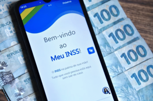 Imagem de um smartphone exibindo a tela de login do aplicativo Meu INSS com dinheiro de cédulas de R$100 ao redor.