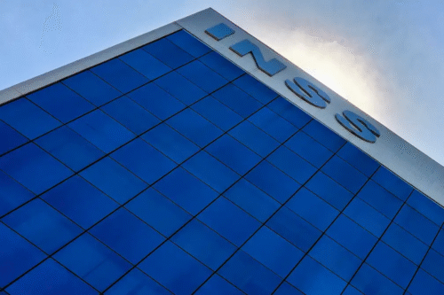 Imagem do edifício da Nissan com fachada de vidros azuis refletindo o céu, visto de baixo, destacando o logotipo da Nissan no topo.
