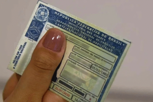 Imagem de uma pessoa segurando uma carteira de motorista brasileira, com detalhes de documentos e validade. A foto destaca a importância de ter documentos essenciais para dirigir no Brasil.