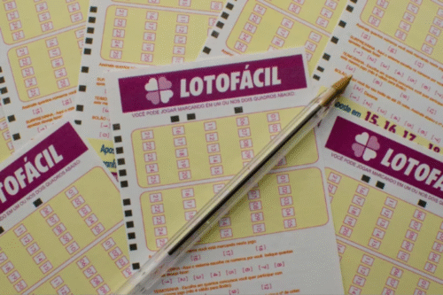 Imagem de bilhetes de loteria 'Lotofácil' com vários bilhetes sobre uma mesa, junto de uma caneta, promovendo jogos de azar e apostas em loteria.