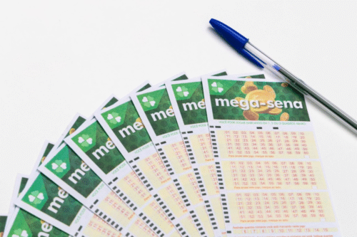 Cartelas de apostas da Mega-Sena com um bolinho de animação, uma caneta azul ao lado, prontos para apostar na loteria.