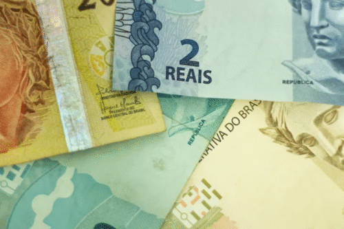 Diversas cédulas de dinheiro brasileiro, incluindo notas de 2, 5 e 20 reais, exibidas de forma sobreposta, simbolizando economia, finanças ou dinheiro.