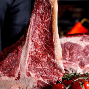 Imagem de um corte de carne bovina, com textura suculenta e marmorizada, preparado para churrasco, decorado com tomates cereja e ramos de alecrim.