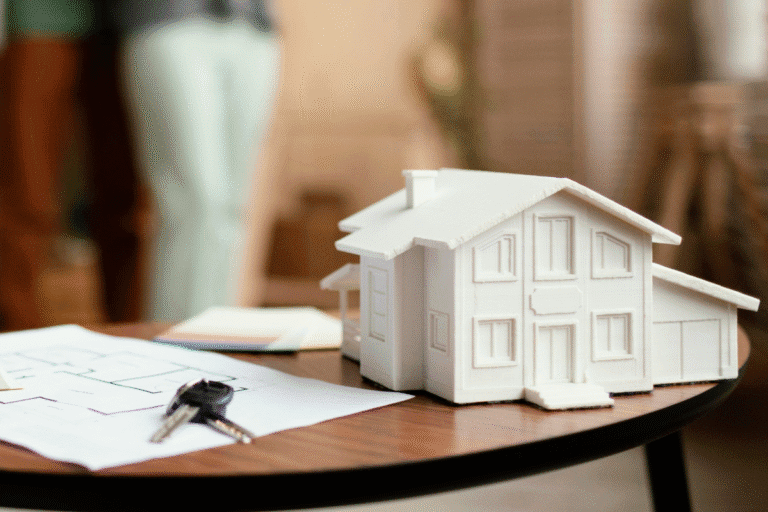 Maquete de uma casa residencial construída em material branco, placements para janelas e portas, sobre uma mesa com documentos e chaves, em ambiente de escritório de arquitetura.