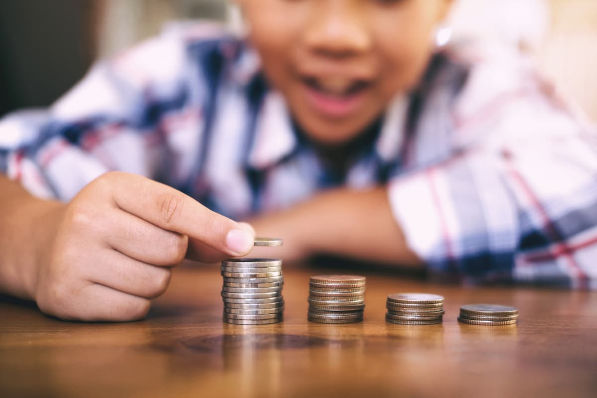 Criança empilhando moedas, representando o conceito de que criança pode investir na bolsa de valores desde cedo.