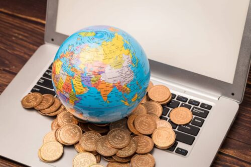 Globo terrestre sobre teclado de notebook com moedas ao redor, representando a diversificação geográfica de investimentos.