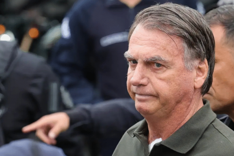 Bolsonaro com expressão séria em primeiro plano, com pessoas ao fundo em ambiente externo.
