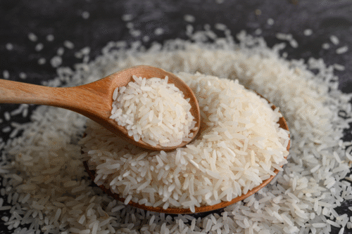 Imagem de arroz branco solto em uma tigela de madeira, com uma colher de pau ao lado, representando arroz branco de alta qualidade para cozinhar.