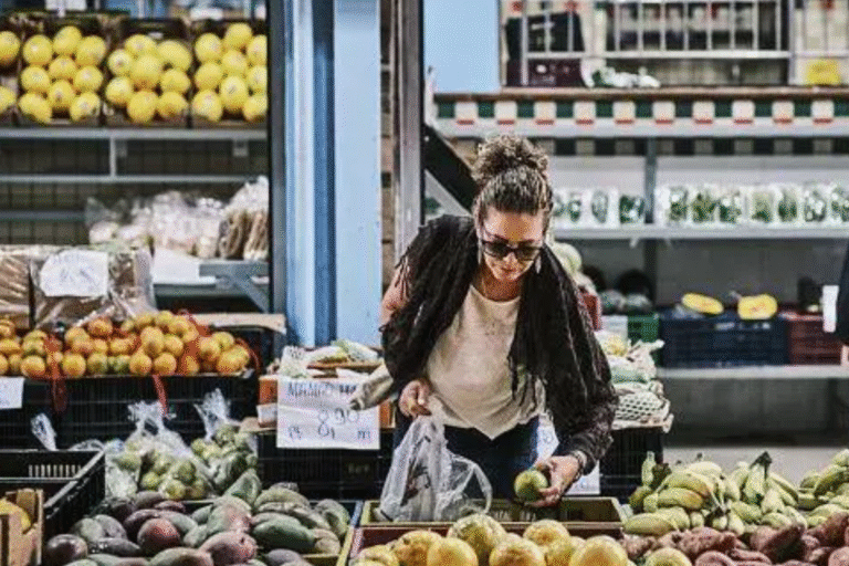 Mulher comprando frutas no hortifrúti do mercado, cercada por bananas, abacates e outras frutas frescas.
