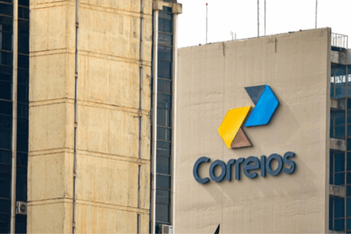 Fachada de uma agência dos Correios com o logo colorido em destaque, em um prédio de edifício comercial no centro urbano.