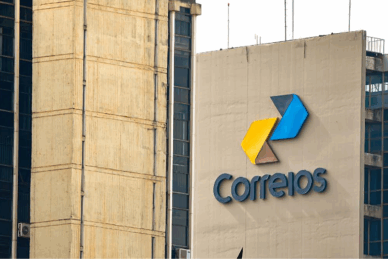 Fachada de uma agência dos Correios com o logo colorido em destaque, em um prédio de edifício comercial no centro urbano.