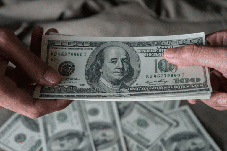 Pessoa trocando uma nota de cem dólares, destaque para a nota com o rosto de Benjamin Franklin, simbolizando dinheiro e valor econômico.