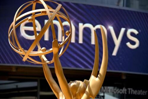 Estatueta do Emmy Awards com fundo de um painel com o nome 'emmys' na parede, em um evento de premiação de televisão.