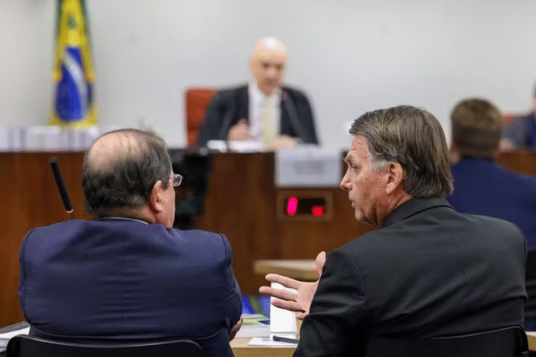 Cena de uma audiência judicial com advogados e juiz em tribunal, destaque para dois Bolsonaro conversando na sessão.