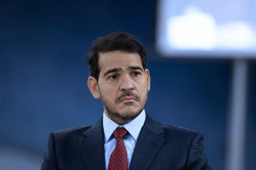 Jorge Messias de terno e gravata vermelha olha pensativo para o lado. Ele tem cabelo curto e escuro e barba aparada. O fundo está desfocado, criando um tom profissional.