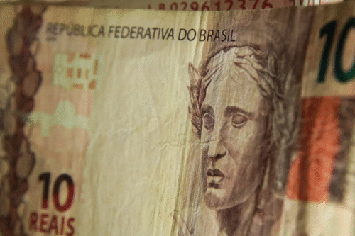 Close de uma nota de 10 reais com um rosto esculpido em relevo. O texto diz "República Federativa do Brasil".