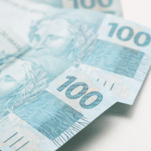 Notas de 100 reais dispostas em uma superfície branca, destacando a linha e detalhes do dinheiro brasileiro.