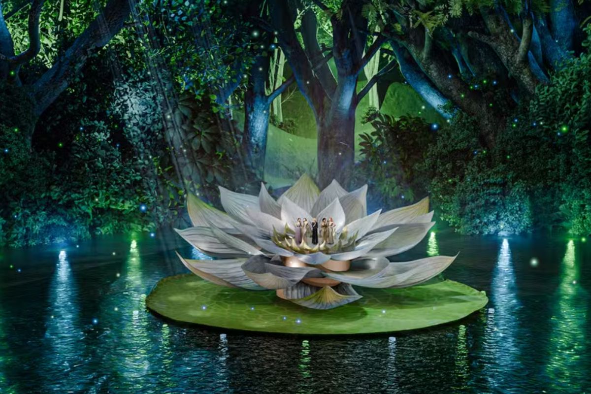 Palco flutuante em um lago com uma Vitória Régia gigante iluminada, rodeada por árvores exuberantes e luzes difusas, criando uma atmosfera encantadora e surreal.