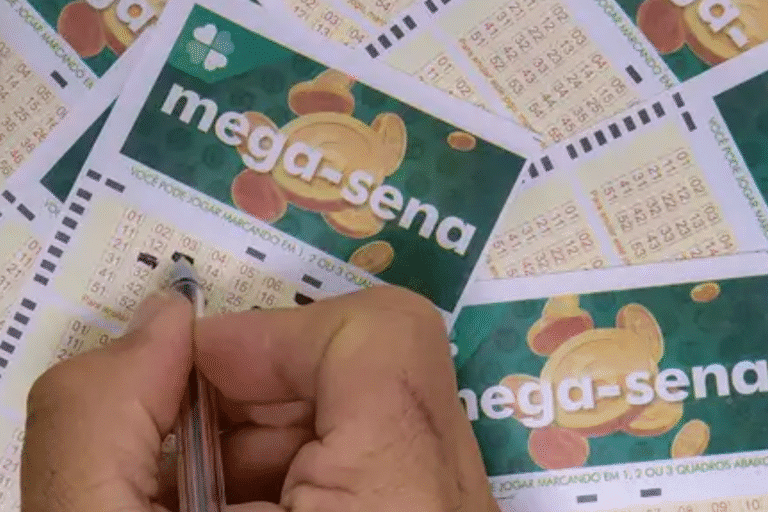 Uma mão marca números em um bilhete de loteria da Mega-Sena, cercada por vários outros bilhetes.