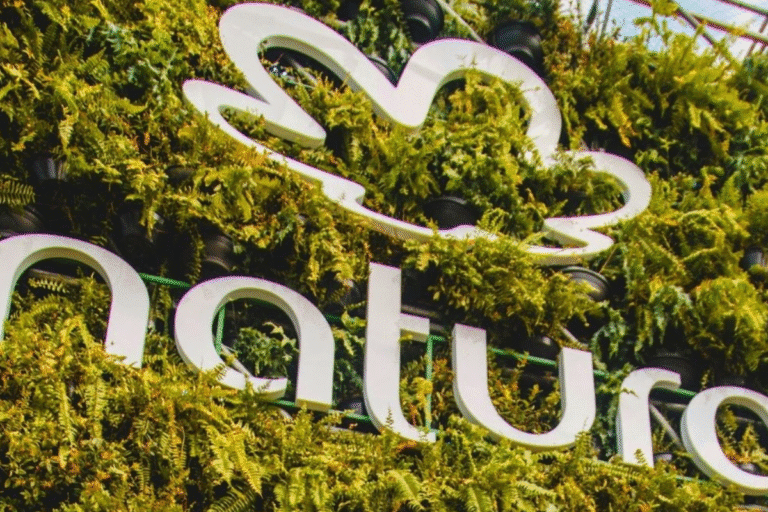 Logo da Natura em destaque com natureza e plantas ao fundo, evidenciando sustentabilidade e conexão com o meio ambiente.