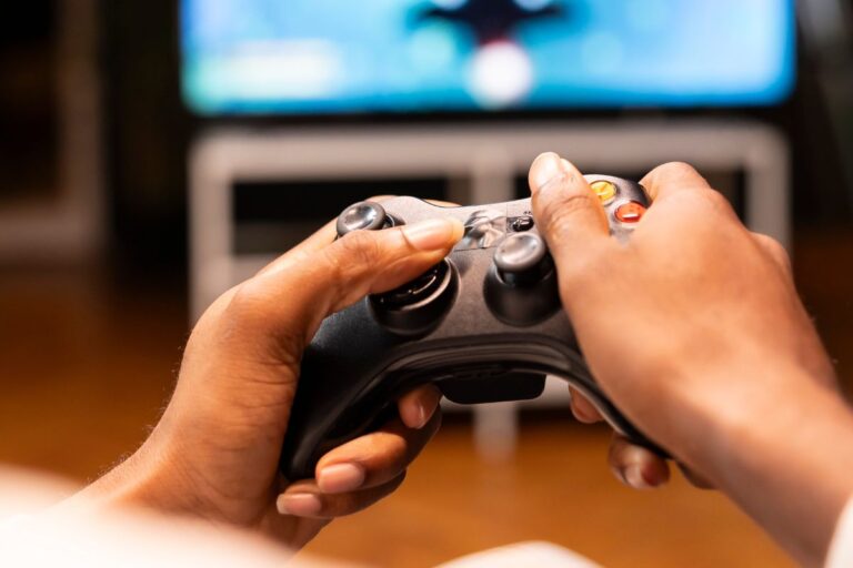 Pessoa segurando um controle de videogame em frente à televisão, jogando um game.