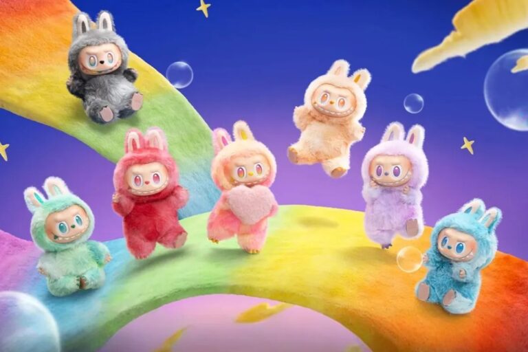 Imagem de sete Labubus coloridos com aparência de coelhinhos, cada um com uma cor diferente, em fundo de céu estrelado e arco-íris, na companhia de pequenas bolhas e estrelas, criando cenário divertido e infantil.