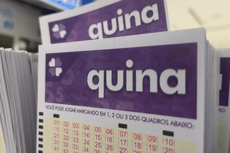 Imagem de uma cartela de loteria Quina com números visíveis, colocada sobre uma superfície. A cartela é roxa com detalhes em branco e textos em preto e vermelho.