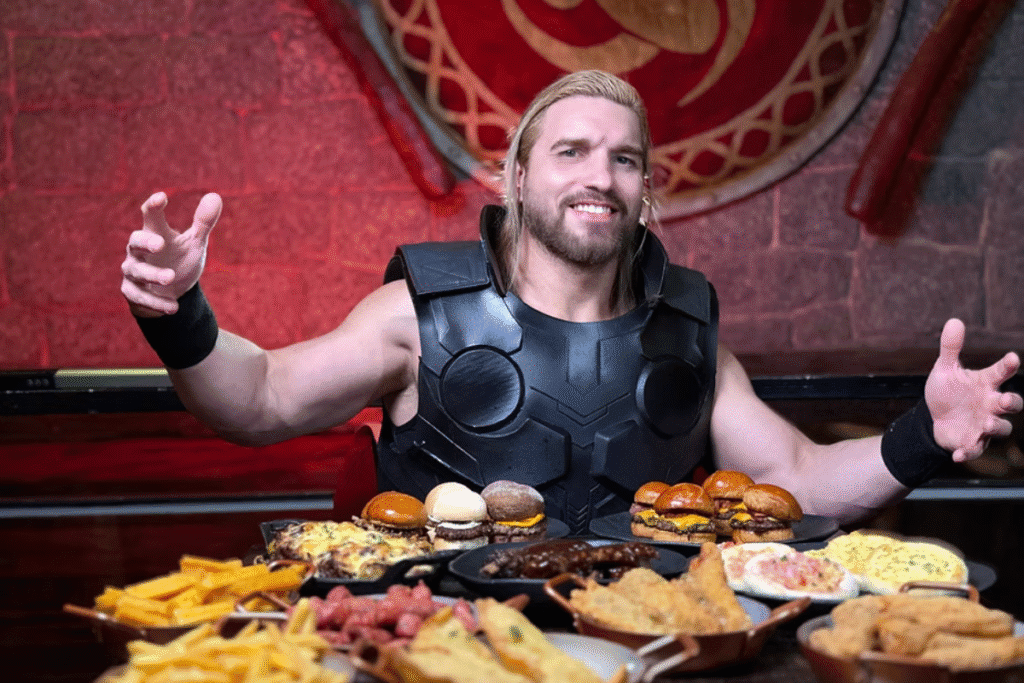 homem viking fantasiado sentado à mesa repleta de pratos variados de comida.