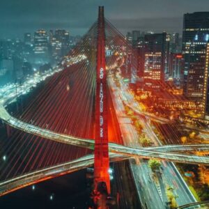 Imagem noturna do Viaduto Santa Paula iluminado na cidade de São Paulo, com o trânsito movimentado e arranha-céus ao fundo, destacando a engenharia e a beleza urbana