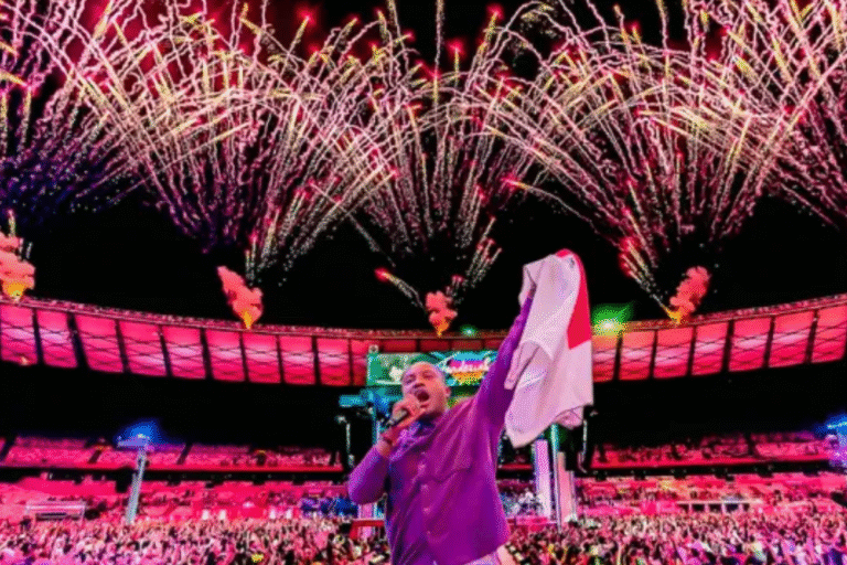 Thiaguinho no palco comemorando uma queima de fogos em um estádio durante um show, com multidão e fogos de artifício no céu.