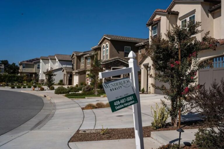 Conjunto de casas residenciais com jardim bem cuidado e um aviso de venda de imóvel da imobiliária Wunderlich Realty em uma rua tranquila.