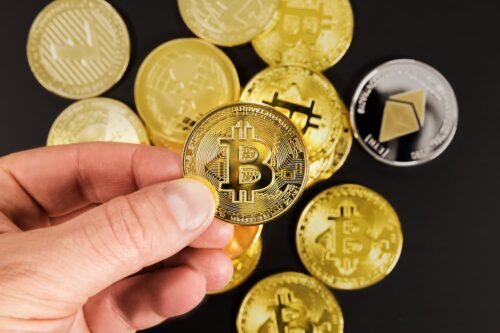 Mão segurando Bitcoin com outras moedas digitais ao fundo, representando as criptomoedas para setembro de 2025.