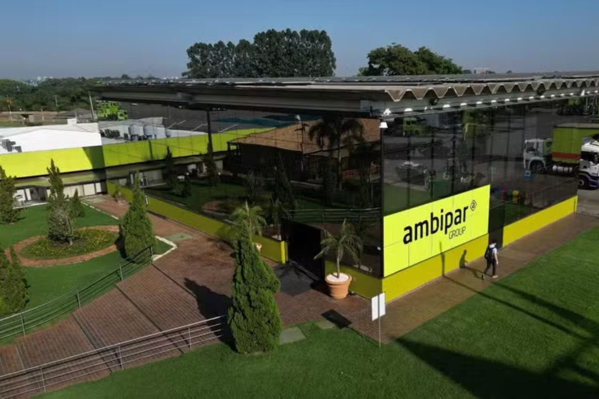 Fachada moderna com vidro espelhado do escritório ambipar group, destaque para o logo amarelo na fachada e ambiente externo bem cuidado com plantas e caminho pavimentado.
