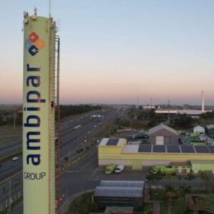 Torre de telecomunicações da Amplibar Group em uma cidade, com várias estradas e construções ao redor ao entardecer, céu claro e horizonte amplo.
