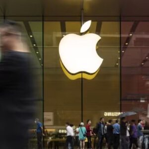 Fachada de uma loja da Apple com grande logotipo iluminado e várias pessoas passando em frente, destacando a presença de consumidores e movimento na área.