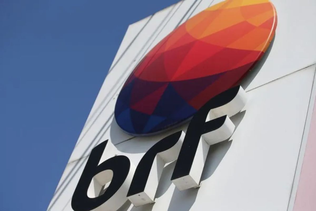 Logo da BRF colorida em relevo, visível em um prédio com fundo de céu azul.