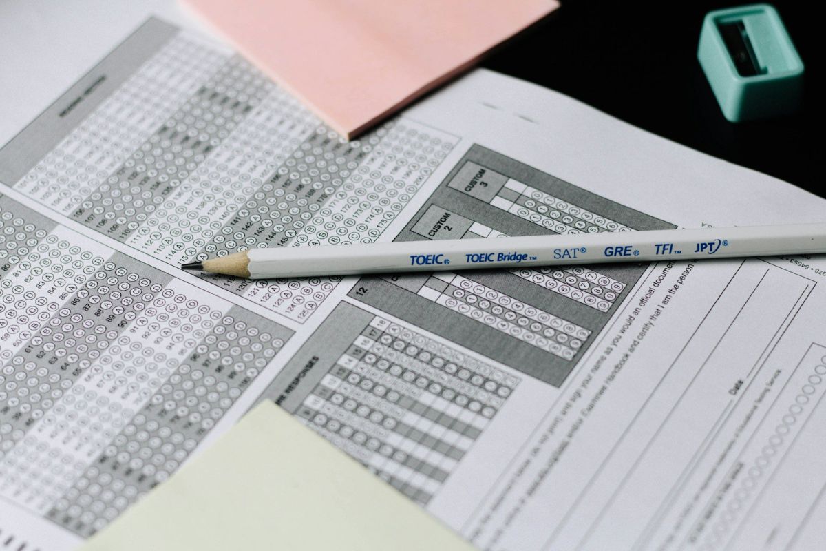 Provas de exames de proficiência, como TOEIC e GRE, com gabaritos, caneta e materiais de estudo em uma mesa de estudo.