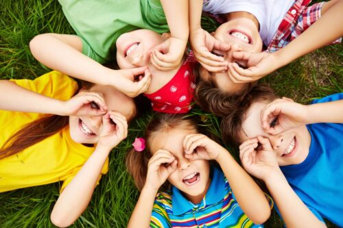 Crianças felizes brincando de esconde-esconde na grama verde ao ar livre, sorrindo e divertindo-se juntas.