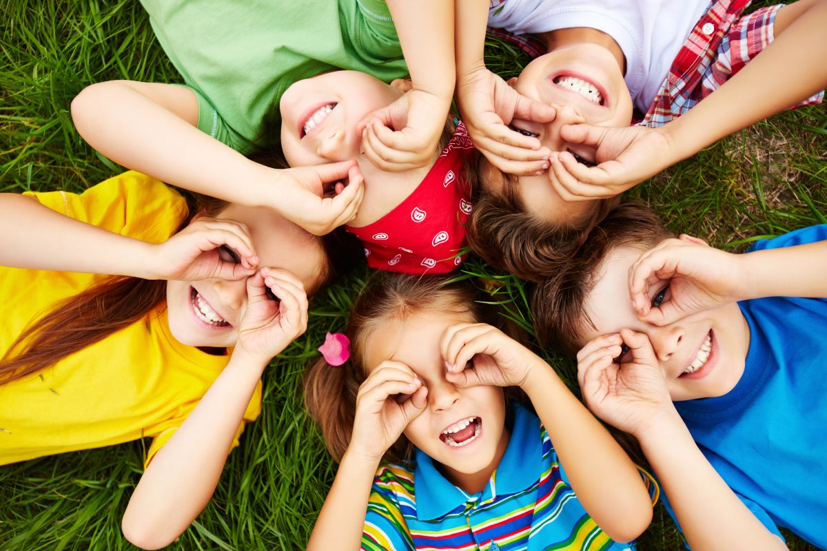 Crianças felizes brincando de esconde-esconde na grama verde ao ar livre, sorrindo e divertindo-se juntas.