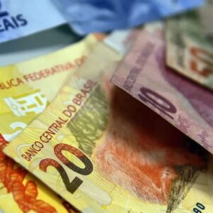Imagem de notas de dinheiro brasileira de diferentes valores, incluindo notas de 2, 10 e 20 reais, espalhadas sobre uma superfície.