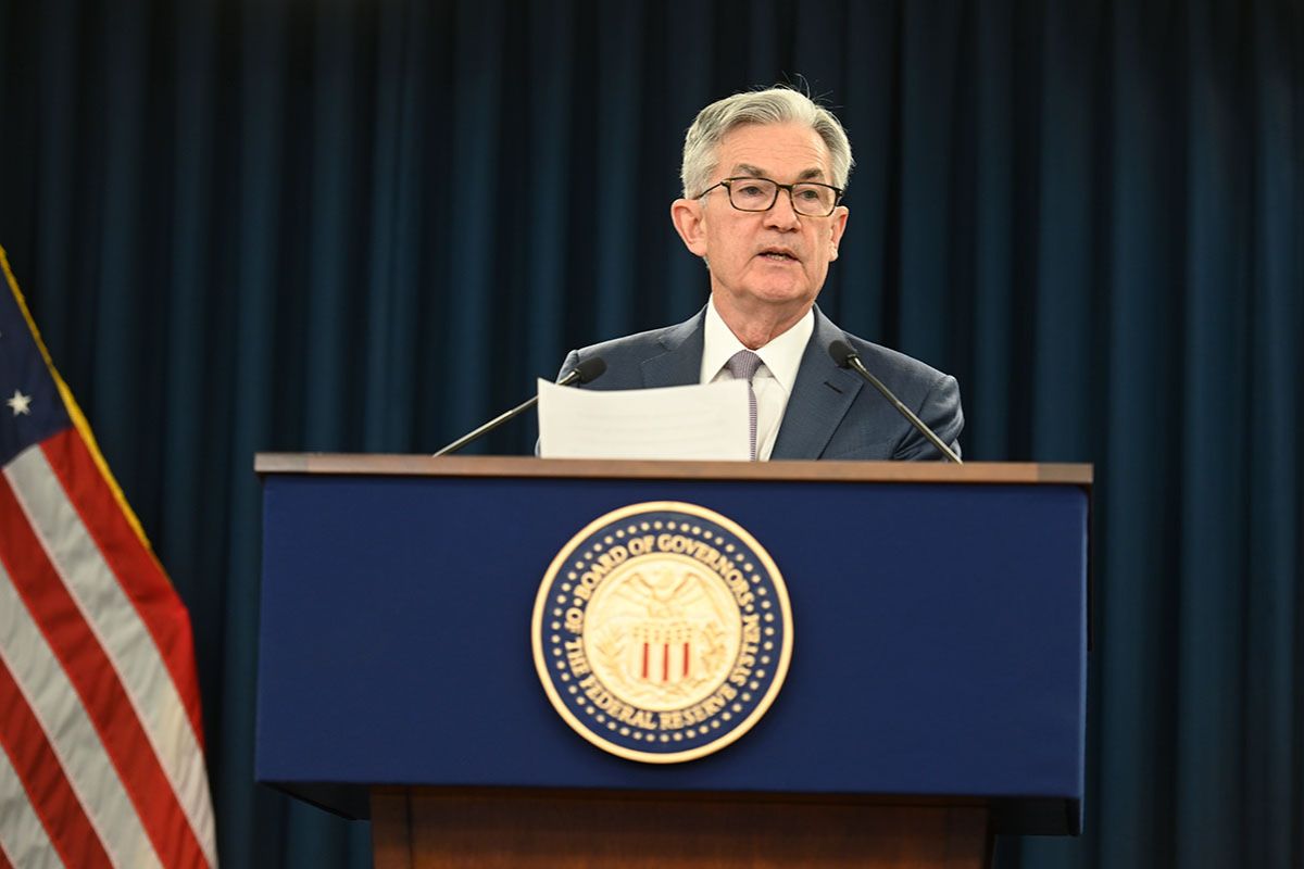 Powell falando em um pódio na posse do presidente dos Estados Unidos, com a bandeira americana ao fundo.